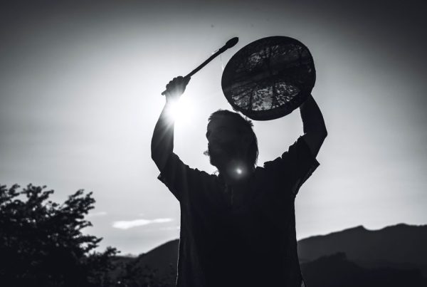 Shamanic healing — A dramatic black-and-white silhouette of a shaman holding a drum against the mountainous backdrop of Lombardia, Italy.