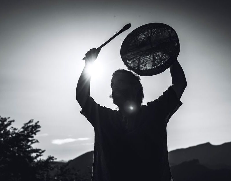 Shamanic healing — A dramatic black-and-white silhouette of a shaman holding a drum against the mountainous backdrop of Lombardia, Italy.