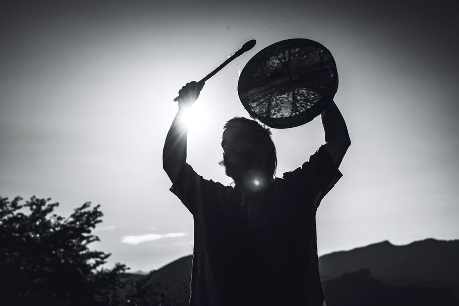 Shamanic healing — A dramatic black-and-white silhouette of a shaman holding a drum against the mountainous backdrop of Lombardia, Italy.